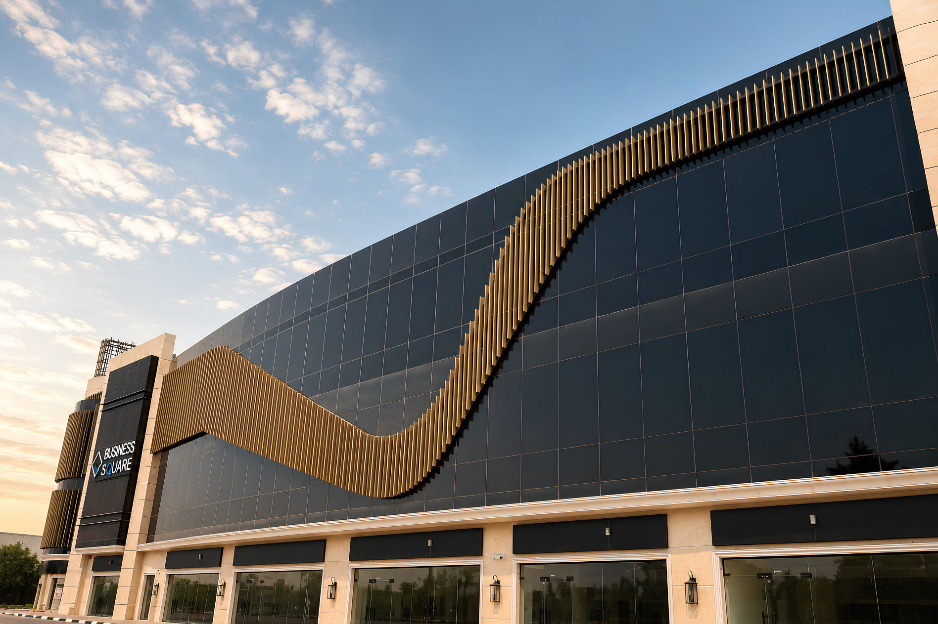 Business Square in Ajman at dusk — a curved glass façade with a bronze fin ribbon, built by Al Telal Building Contracting